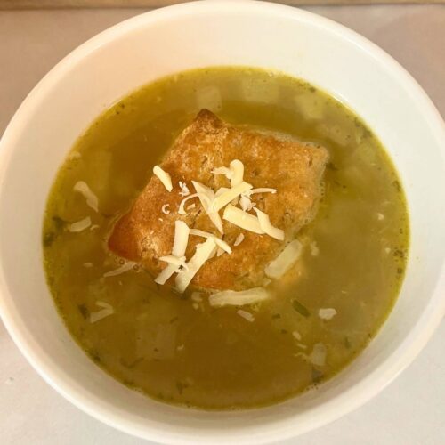 A white bowl of vegetable soup that has a biscuit and shredded cheese on top.