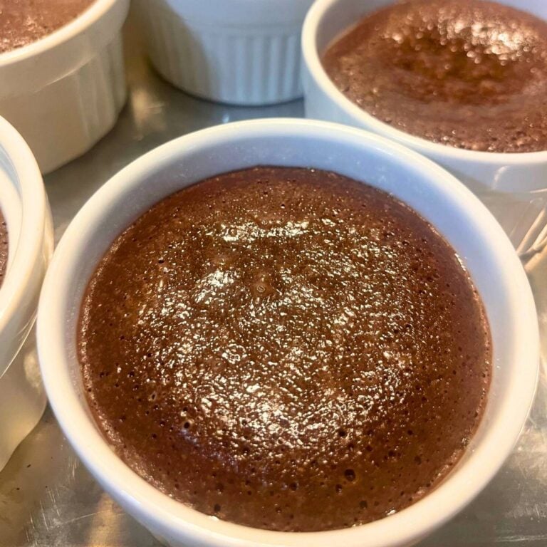 A white ramekin of chocolate lava cake on a stainless steel sheet pan.