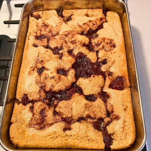 A 9x13 stainless steel pan of cooked strawberry cobbler, sitting on a stove.