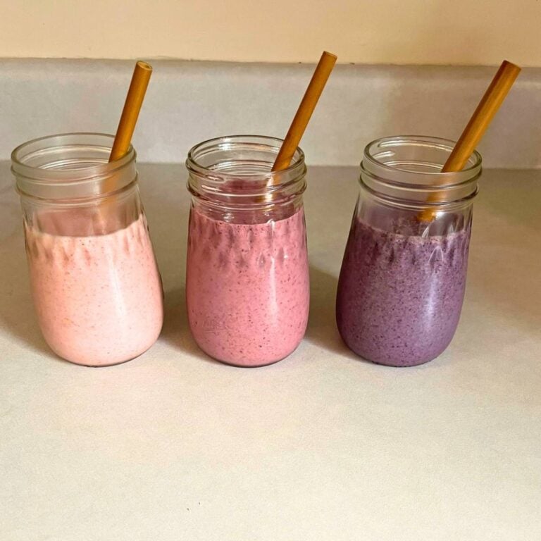 Three glasses of healthy smoothie recipes sitting on a kitchen counter with bamboo straws in each one.