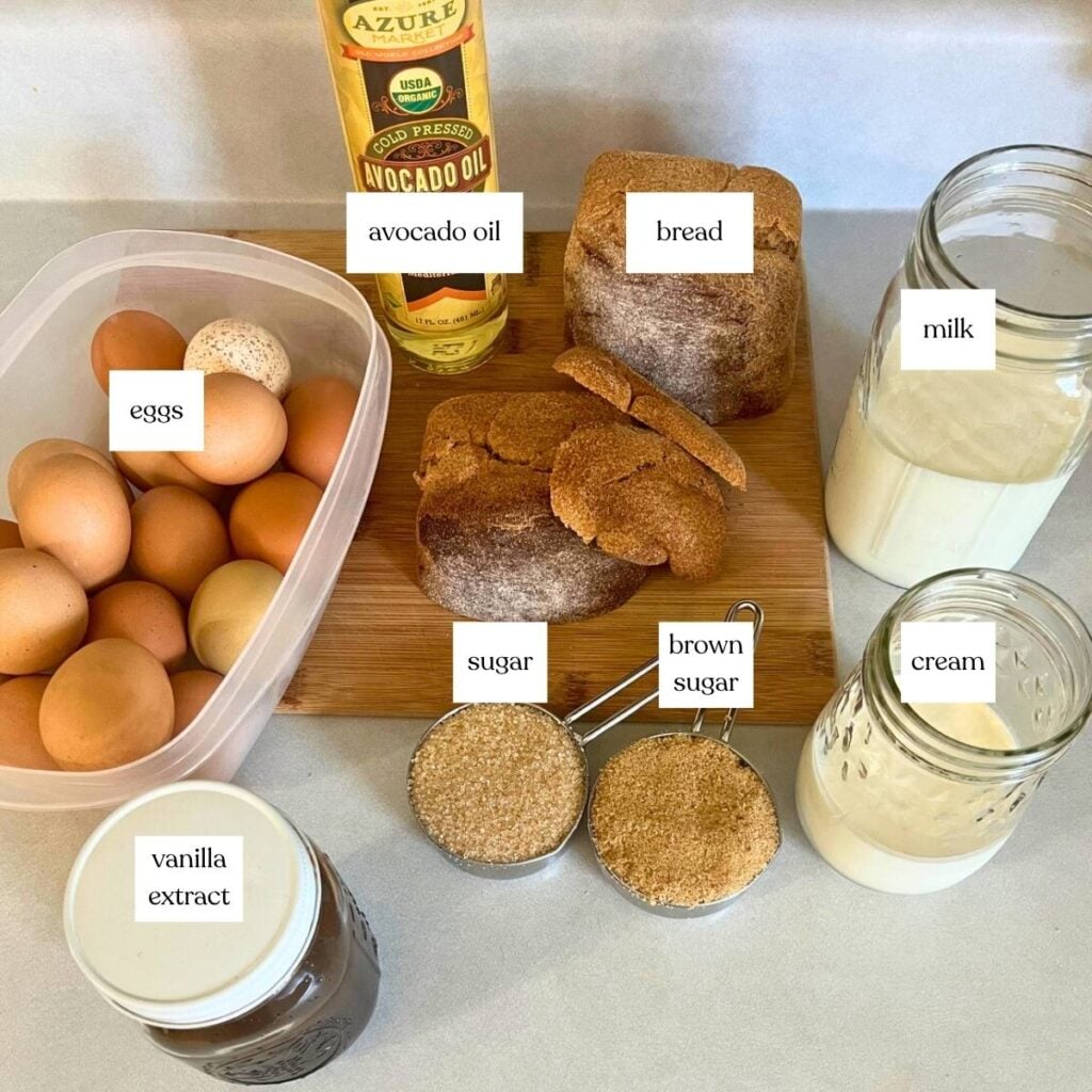 Ingredients for making French toast casserole sitting on a counter. Pictured from left to right and back to front are eggs, avocado oil, bread, milk, granulated sugar, brown sugar, cream, and vanilla extract.