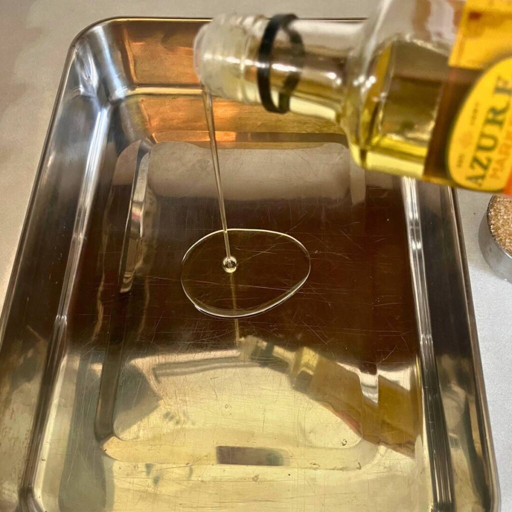 Woman pouring avocado oil in a 9x13 stainless steel pan.
