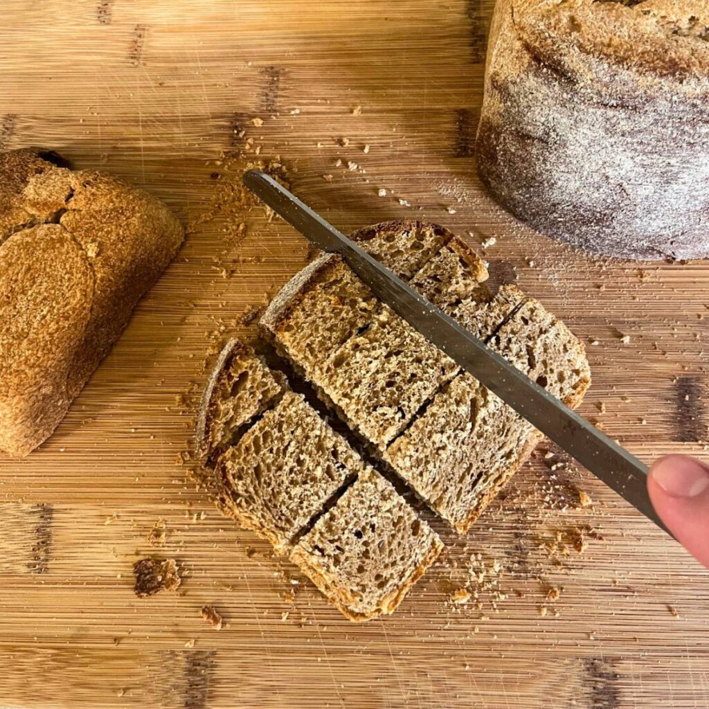 Woman cutting bread into roughly one inch cubes on a wood cutting board.