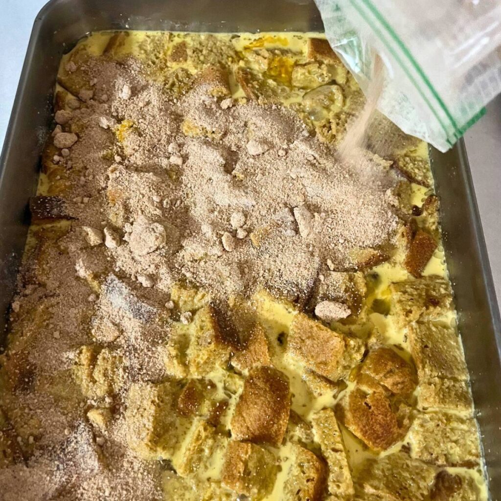Woman sprinkling a sweet topping over an uncooked French toast casserole in a 9x13 pan.